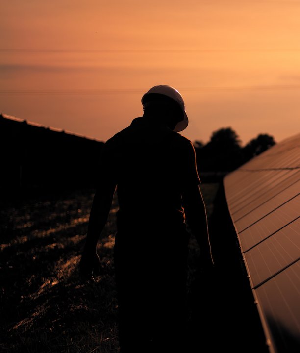 Worker walking next to solar panels at sunset.