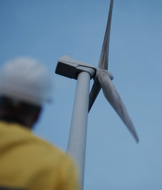 Worker looking up at a windmill under a blue sky.